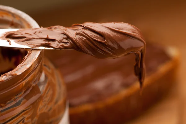 Faca cheia de nougat chocolate doce espalhar no frasco de vidro . — Fotografia de Stock