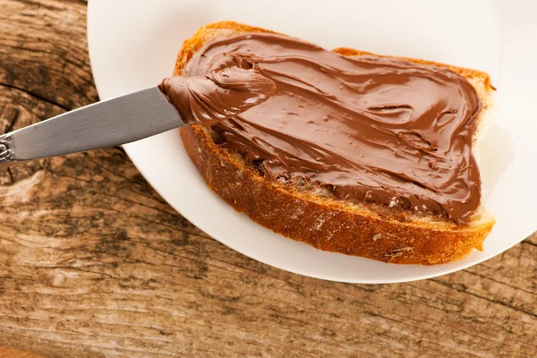 Fatia de pão com nougat de chocolate doce espalhada no prato branco — Fotografia de Stock