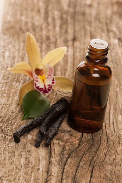 Gousses de vanille, huile d'aromathérapie et fleurs d'orchidée sur le dos en bois — Photo