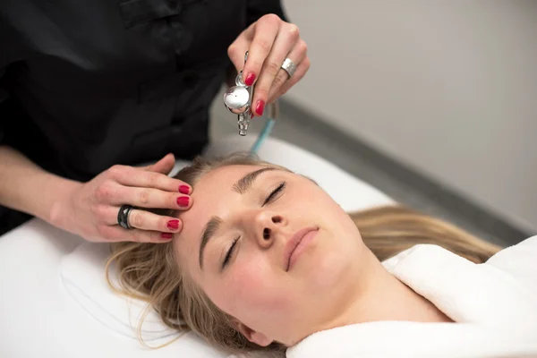 Mujer joven acostada en la mesa de masaje recibiendo masaje facial. Beaut. — Foto de Stock