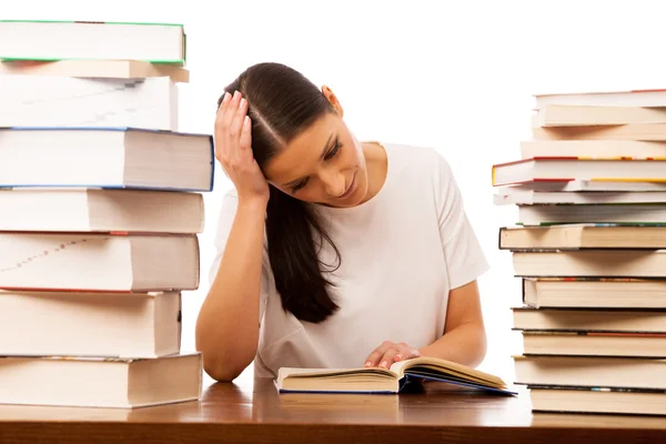 Verveeld vrouw achter de tafel tussen twee stapel boeken lezen. — Stockfoto