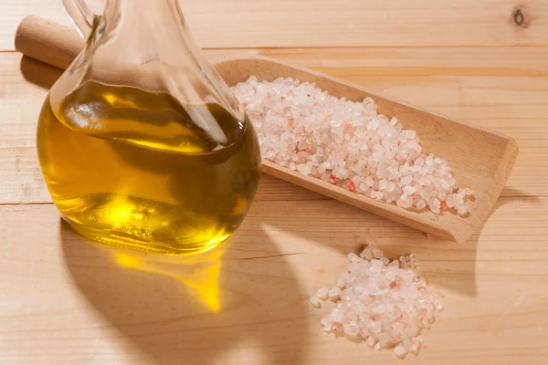 Cuchara de madera llena de sal de piedra y aceite de oliva sobre una mesa — Foto de Stock