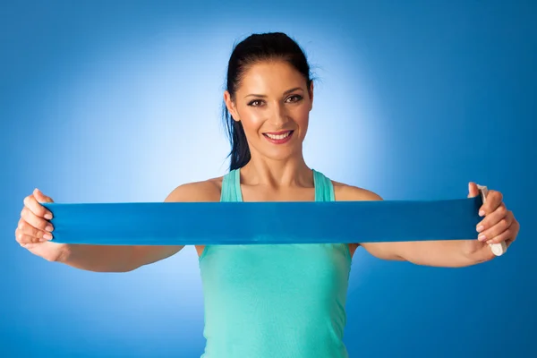 Woman working out with band in fitness gym over blue background — Stock Photo, Image
