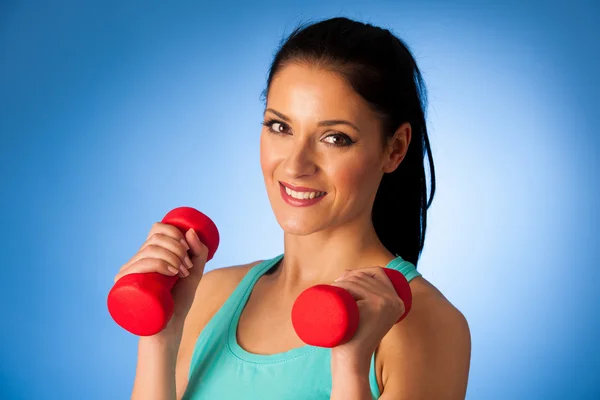 Active woman with dumbbells workout in fitness gym over blue bac — Stock Photo, Image