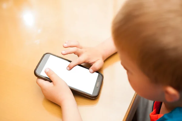 Niño juega con un teléfono inteligente en la mesa de la cocina — Foto de Stock