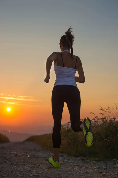 Mujer corriendo en un camino de montaña al atardecer de verano —  Fotos de Stock