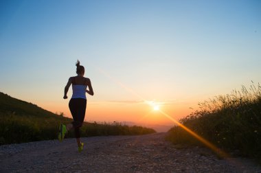 woman running on a mountain road at summer sunset clipart