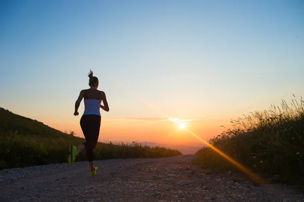 Vrouw draait op een bergweg bij zonsondergang zomer — Stockfoto