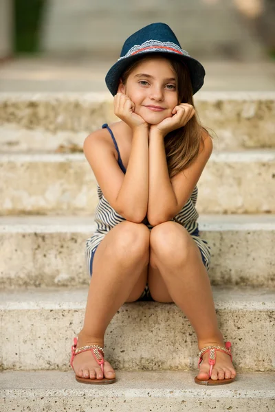 Cute young girl with hat sitting on stairs in park — Stock Photo, Image