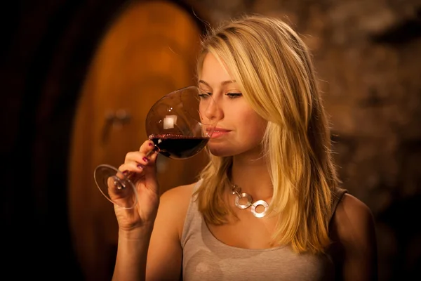 Schöne junge blonde Frau verkostet Rotwein in einem Weinkeller — Stockfoto