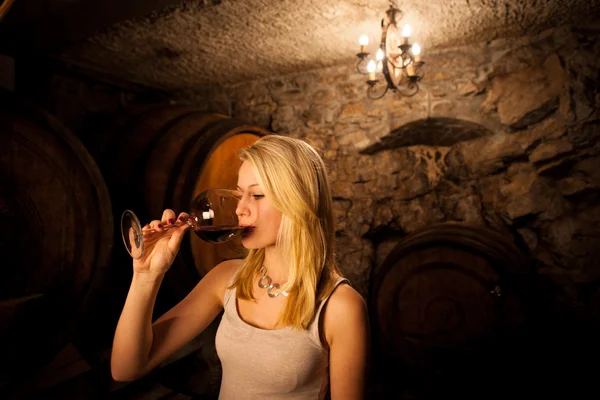 Schöne junge blonde Frau verkostet Rotwein in einem Weinkeller — Stockfoto