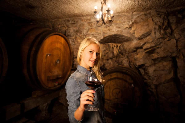 Schöne junge blonde Frau verkostet Rotwein in einem Weinkeller — Stockfoto