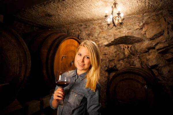 Schöne junge blonde Frau verkostet Rotwein in einem Weinkeller — Stockfoto