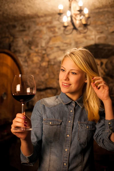 Schöne junge blonde Frau verkostet Rotwein in einem Weinkeller — Stockfoto