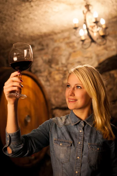 Schöne junge blonde Frau verkostet Rotwein in einem Weinkeller — Stockfoto