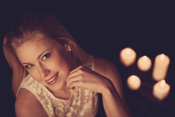 Young blonde woman on black sheets with candels in background — Stock Photo, Image