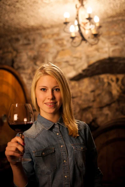 Schöne junge blonde Frau verkostet Rotwein in einem Weinkeller — Stockfoto