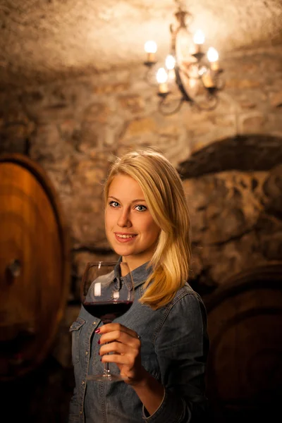 Schöne junge blonde Frau verkostet Rotwein in einem Weinkeller — Stockfoto