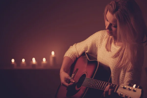 Giovane donna bionda che suona la chitarra a lume di candela — Foto Stock