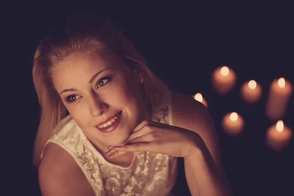 Young blonde woman on black sheets with candels in background — Stock Photo, Image