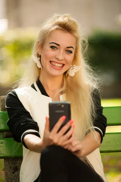 Blonde woman with smart phone on a bench in park — Stock Photo, Image