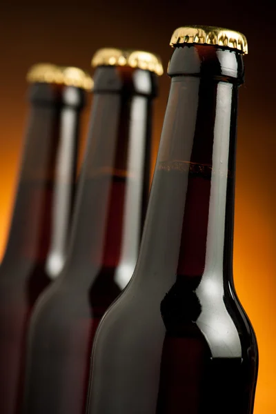 Три коричневые бутылки пива стоят в ряд на оранжевом фоне — стоковое фото