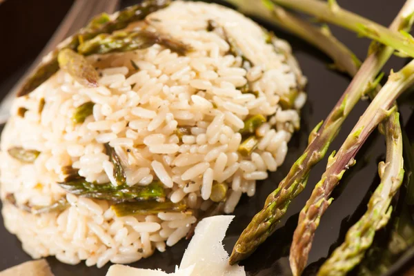 Riz aux asperges sauvages sur une assiette noire à la fourchette servie sur un — Photo