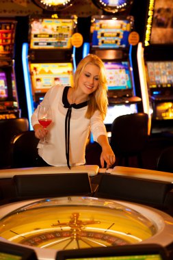Young blond woman playing roulette in casino and winning clipart