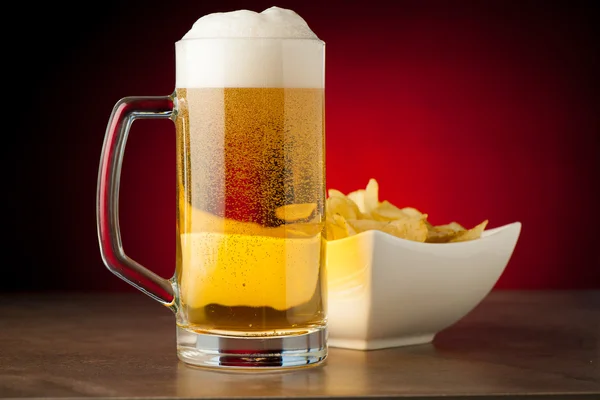 Bottle, glass of beer and potatoe chips on stone table over red — Stock Photo, Image