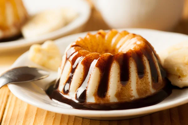 Vanilla pudding with dessert with chocolate syrup and banana slices on white plate served on wooden table — Stock Photo, Image