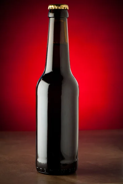 Bottle of beer on a stone table over red background — Stock Photo, Image