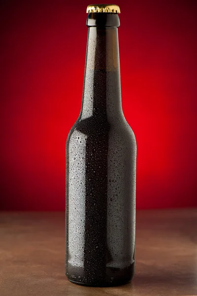 Бутылка пива с капельками воды на каменном столе над красным бэкгром — стоковое фото