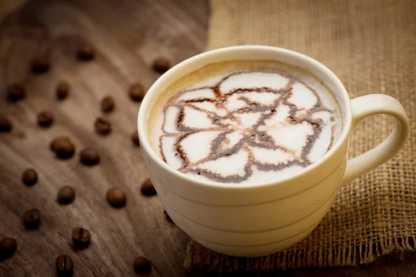 Filiżankę cappuccino doręczane drewniany stół z ziaren kawy w th — Zdjęcie stockowe