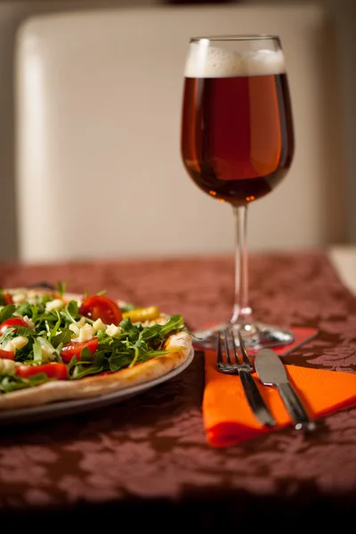Пицца с руколой, помидорами черри и бокалом пива на тебле — стоковое фото