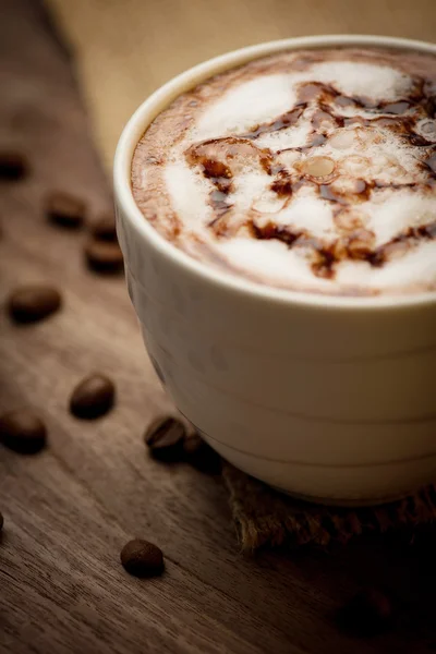 Cup af cappuccino serveret på træbord med kaffebønner i th - Stock-foto