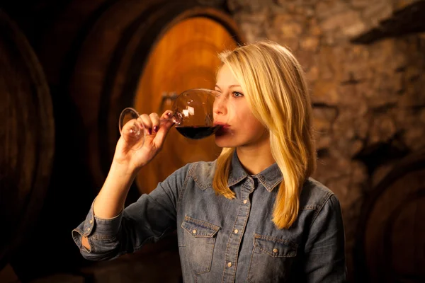 Schöne junge blonde Frau verkostet Rotwein in einem Weinkeller — Stockfoto