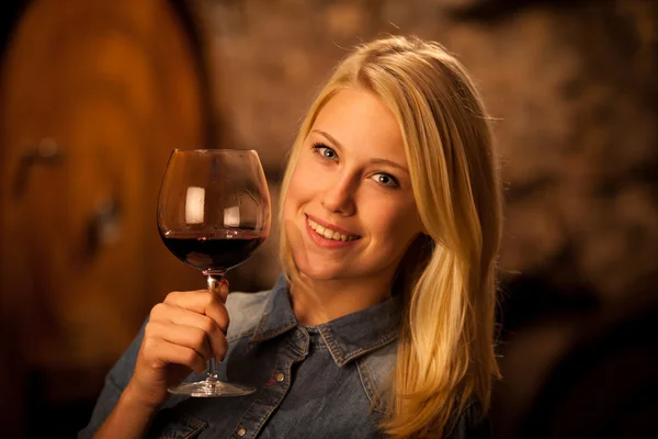 Belle jeune femme blonde dégustant du vin rouge dans une cave à vin — Photo