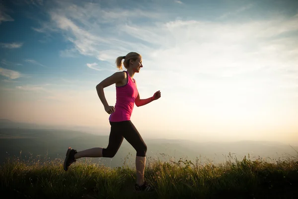 Hermosa joven corre a través del país en un camino de montaña en —  Fotos de Stock