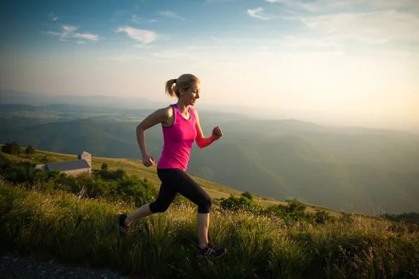 Bella giovane donna corre attraverso il paese su un sentiero montuoso a — Foto Stock