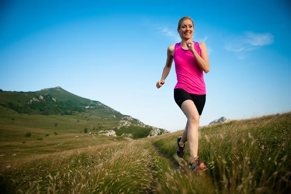 Hermosa joven corre a través del país en un camino de montaña en — Foto de Stock