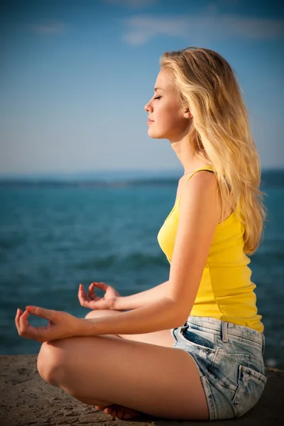 Mulher loira jovem bonita meditando em uma praia ao nascer do sol em — Fotografia de Stock