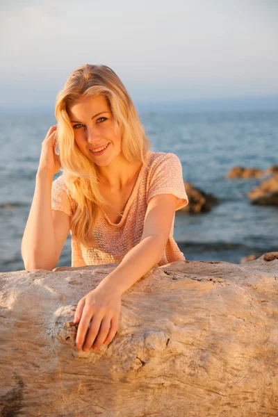 Schöne junge blonde Frau, die sich in der frühen Abenddämmerung am Strand ausruht — Stockfoto