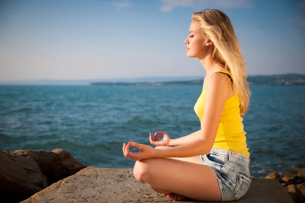 Hermosa joven rubia meditando en una playa al amanecer en — Foto de Stock