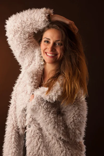 Брюнетка танцівниця позує в білому пухнастому пальто перед темним тлом — стокове фото