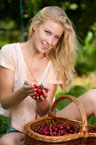 Mooie jonge blonde vrouw oogsten kersen op een hete lente — Stockfoto
