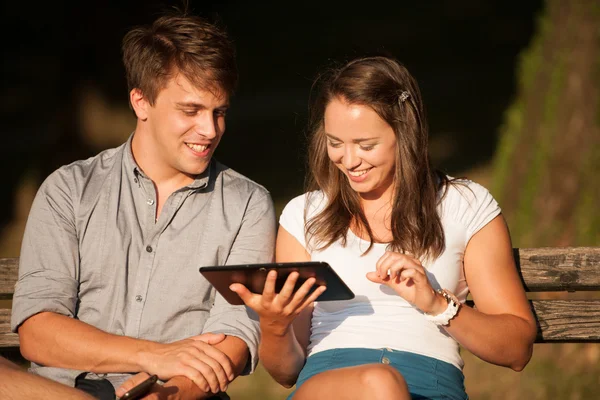 Young couple having fun on a bench in park while socializing ove — Stock Photo, Image