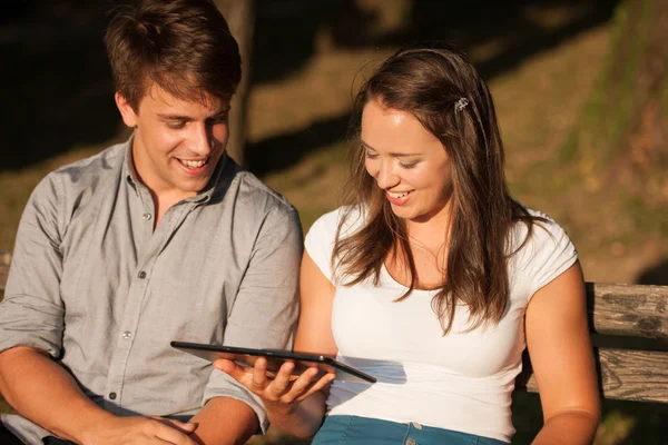 Pareja joven divirtiéndose en un banco en el parque mientras socializa ove — Foto de Stock