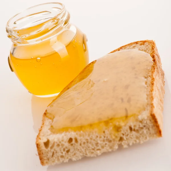Mel dourado pegajoso doce em uma fatia de pão fresco e um copo — Fotografia de Stock