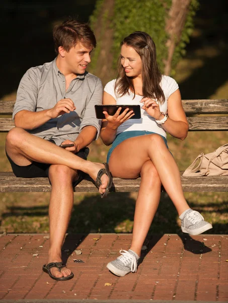 Pareja joven divirtiéndose en un banco en el parque mientras socializa ove — Foto de Stock