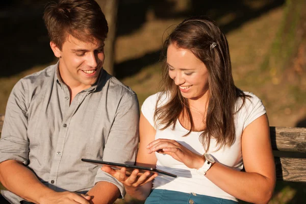 Pareja joven divirtiéndose en un banco en el parque mientras socializa ove — Foto de Stock